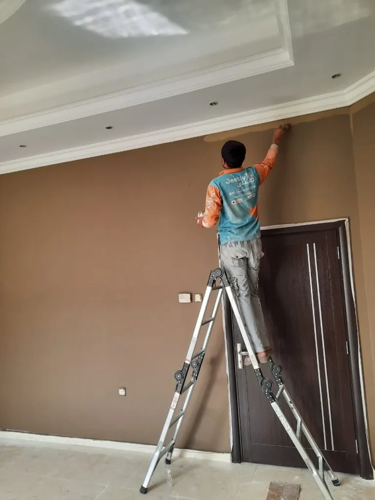 Painter on a ladder finishing walls around a door frame